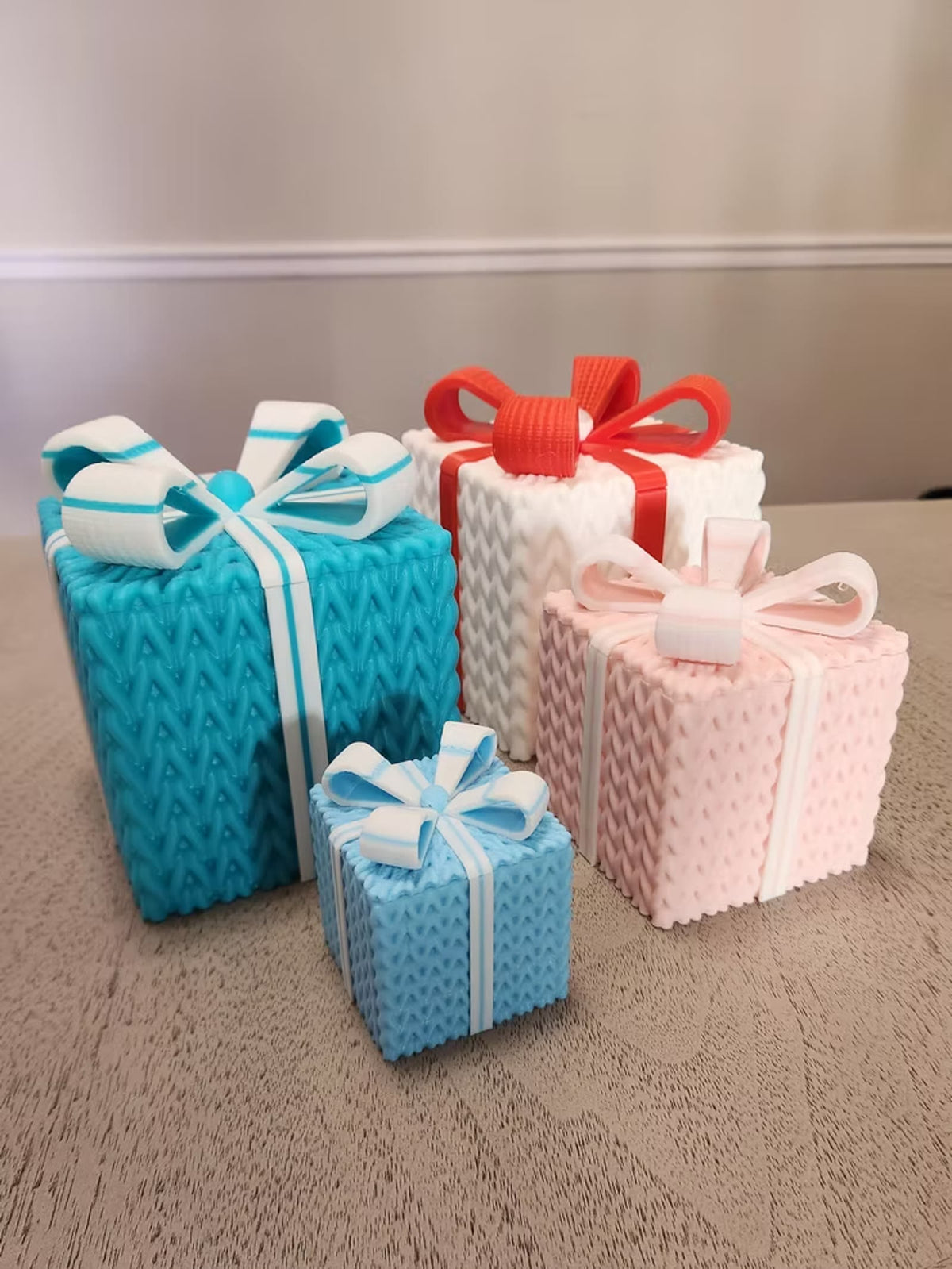 Four knitted gift boxes with bows in teal, white, pink, and light blue
