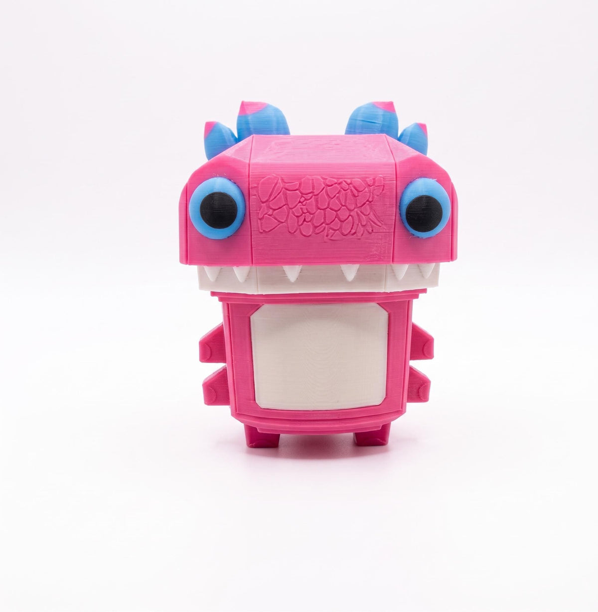 May include: A pink creature figurine with a blocky head and body. It features large blue eyes, a white rectangular chest panel, and white teeth. The top of the head has blue and pink spikes, and the surface shows a textured, layered 3D printed finish.